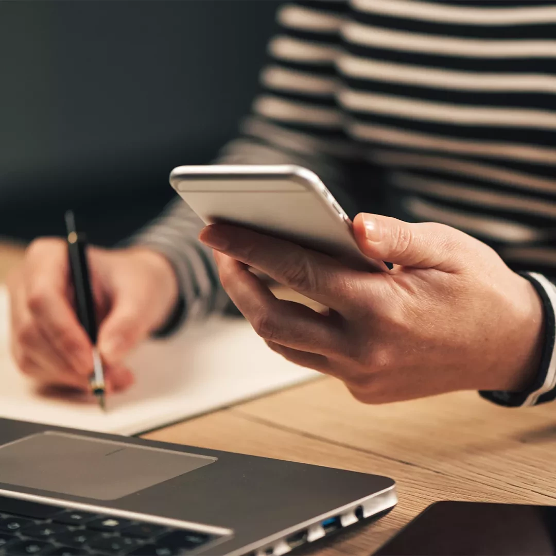 Person using their smartphone and writing on paper